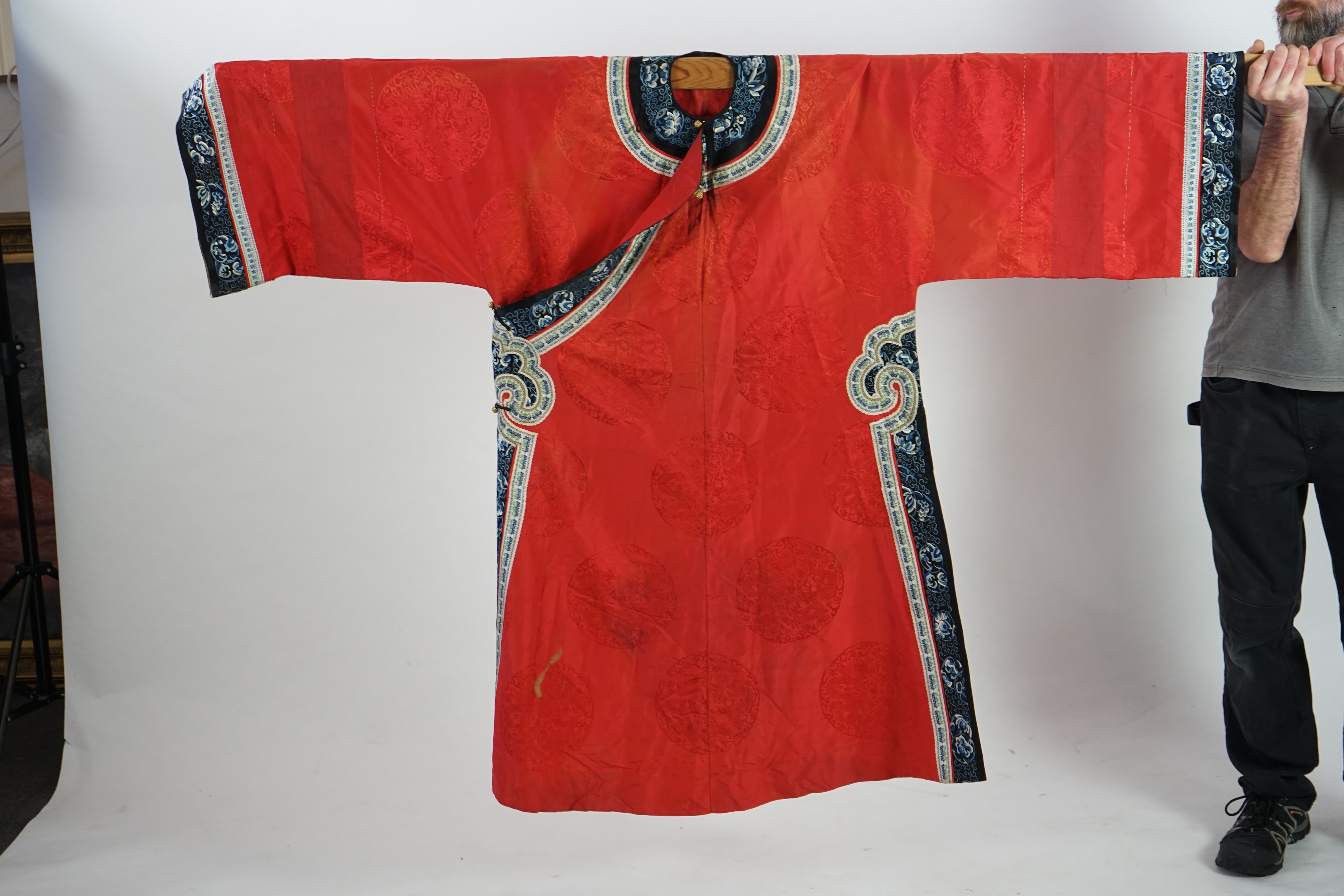 A late 19th century Chinese Manchu ladies red silk damask robe, with black and blue silk embroidered borders, ornately edged cream floral silk braiding, length from neck (back) to bottom edge 132cm long. Condition - stai